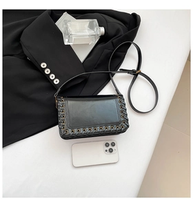 Detail of black crossbody bag with gold eyelets and woven strap on a white background
