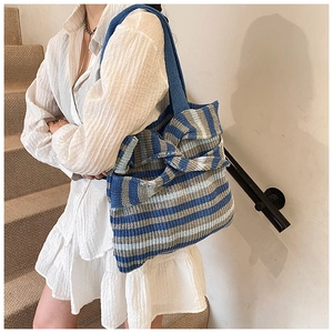Detail of striped knit tote bag with large bow decor worn over the shoulder by a model