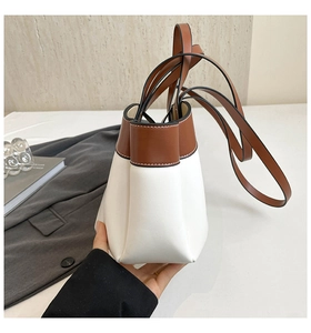 Detail view of a minimalist white and brown bucket bag with long leather shoulder straps