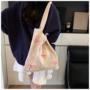 Gros plan d'un sac cabas en crochet beige avec des nœuds roses en relief et texture maille