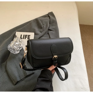 Detail of black pebbled leather crossbody bag with elegant gold hardware and flap closure