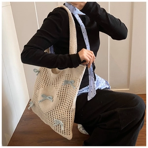 Détail du sac cabas en tricot crème avec nœuds bleus et poche cœur porté en bandoulière