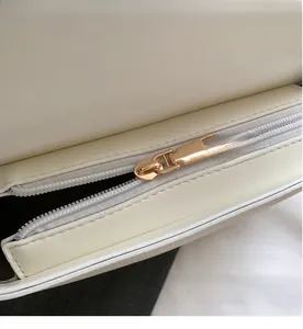 Macro shot of smooth gold zipper and white litchi grain leather on a shoulder bag