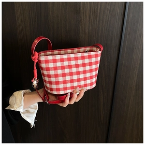 Detail of red gingham canvas bag with metallic charm and knot on leather strap