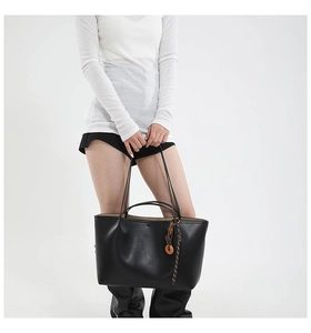 Detail of black trapezoid tote bag with wooden charm and striped ribbon accent