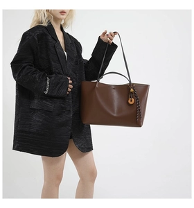 Detail of dark brown leather tote bag with unique woven charm shown on model
