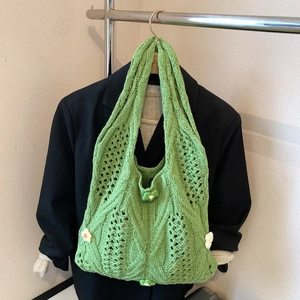 Sac bandoulière en tricot vert avec fleurs blanches exposé sur un blazer noir