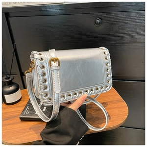Silver square leather handbag with woven eyelet edges and gold hardware on wood background