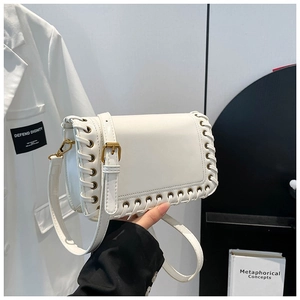 Chic white square crossbody bag with laced edges and gold hardware held against a suit