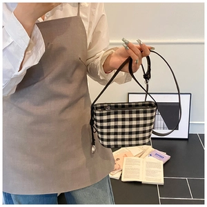 Detail of checkered canvas tote bag with silver zipper and slim black leather strap