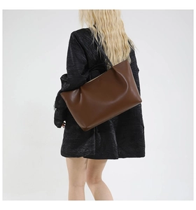 Detail of a large brown matte tote bag with slim black straps worn by a model in black