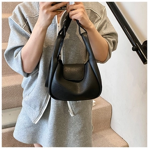 Detail of black tote bag with litchi grain leather texture and magnetic flap closure