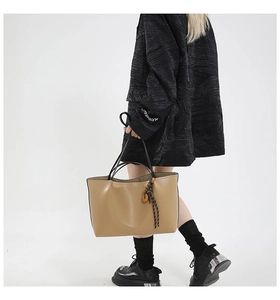 Khaki faux leather tote bag with black double handles and wood charm shown on model
