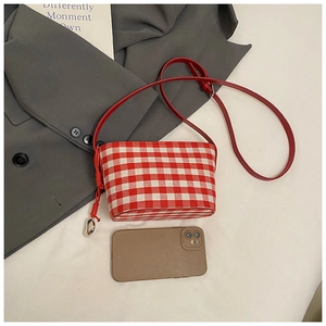 Detail of red gingham fabric bag with leather strap, heart pendant and phone for scale