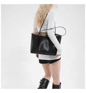 Side view of a large black minimalist leather tote bag worn by a model for daily commute