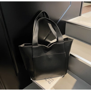 Detail of minimalist black tote bag with textured leather on gray steps and books