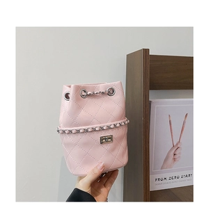 Detail of pink quilted bucket bag featuring a silver twist lock and woven chain strap
