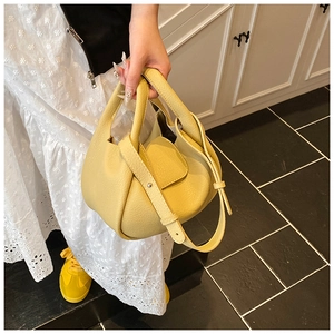Detail of yellow lychee grain leather bucket bag with wide handle shown with white dress