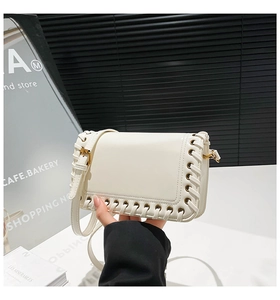Close-up of white woven square bag with gold eyelets and adjustable shoulder strap