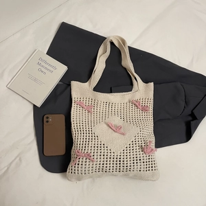 Sac fourre-tout en tricot crème avec nœuds roses et motif cœur sur fond de literie épuré