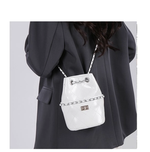 Detail shot of white quilted bucket bag with silver chain strap on a model's shoulder