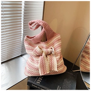 Dettaglio della borsa tote in maglia a righe rosa e beige con grande fiocco su libro d'arte