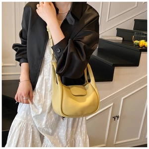 Detail of light yellow pebble leather handbag featuring a smooth curved flap and shoulder strap