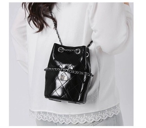 Detail of black quilted bucket bag featuring a silver chain strap and metal turn-lock