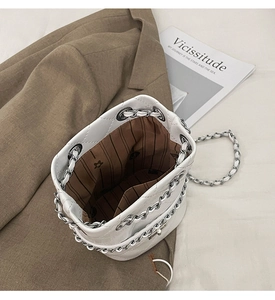 Close-up of a white quilted bucket bag showing striped lining and metal chain strap