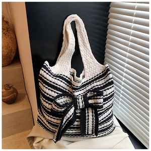 Dettaglio della borsa tote a righe in maglia con fiocco nero in luce naturale calda