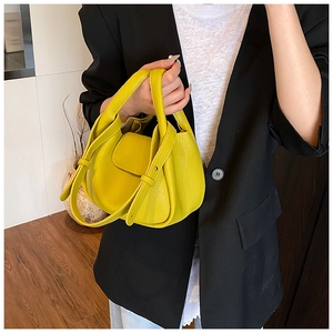Detail of bright yellow tote bag with lychee texture held by a model in a black blazer