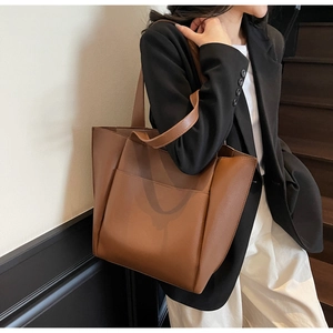 Detail of a large brown tote bag with an external pocket worn by a model in a suit