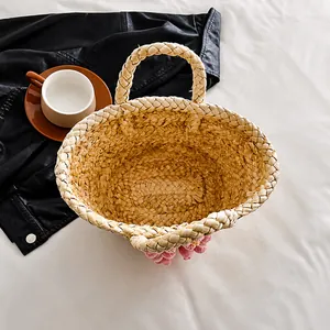 Dettaglio della borsa in paglia intrecciata con ciondolo a fragola rosa su lenzuola bianche
