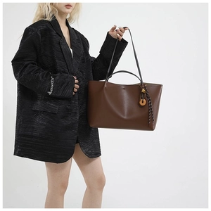 Minimalist large brown leather tote bag with decorative pendant worn by a model
