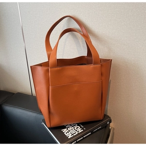 Detail of a brown faux leather tote bag showing fine texture and front pocket on a sofa