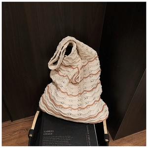 Close-up of beige knitted shoulder bag with orange wave patterns on a dark wooden background