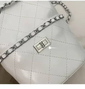 Close-up of white quilted leather texture with silver metal twist lock and chain strap