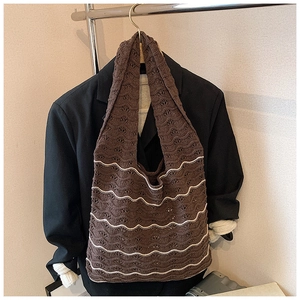 Close-up of brown knit shoulder bag with white wavy patterns on a dark suit background