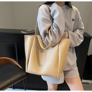 Detailed view of beige pebble grain leather tote bag worn by model in casual setting