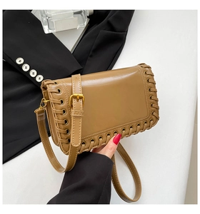 Detailed view of brown woven shoulder bag with metallic eyelets and gold hardware