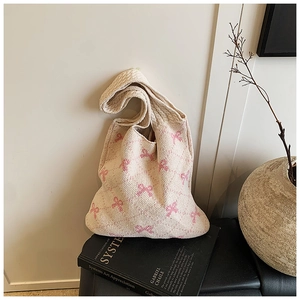 Detail of cream knit tote bag featuring pink bow patterns on a minimalist indoor display