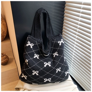 Detail shot of black knitted tote bag featuring white bows and soft woven texture