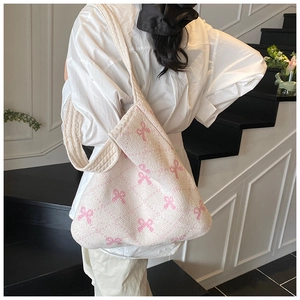 Detail of white knit tote bag featuring pink bow patterns and wide comfortable shoulder strap