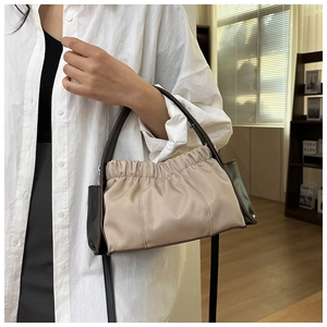 Detail einer beigen Falten-Schultertasche mit schwarzem Besatz, getragen von einem Model