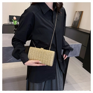 Borsa a mano in paglia color champagne con sottile tracolla a catena indossata da modella