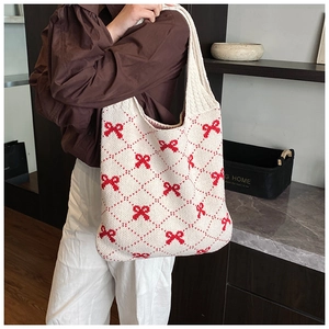 Detail of knitted tote bag with red bow pattern carried by a model in casual setting