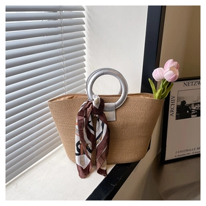 Macro shot of woven straw handbag with silver ring handle and silk scarf detail