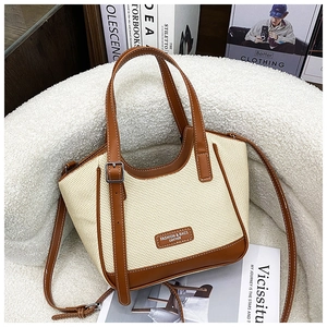 Détail du sac à bandoulière en toile et cuir marron sur un support en peluche blanche