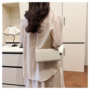 Dettaglio di una pochette in paglia intrecciata beige con sottile tracolla a catena