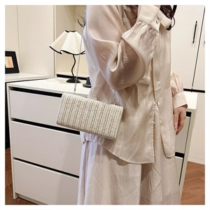Dettaglio pochette in paglia beige con trama a V e tracolla a catena argento elegante